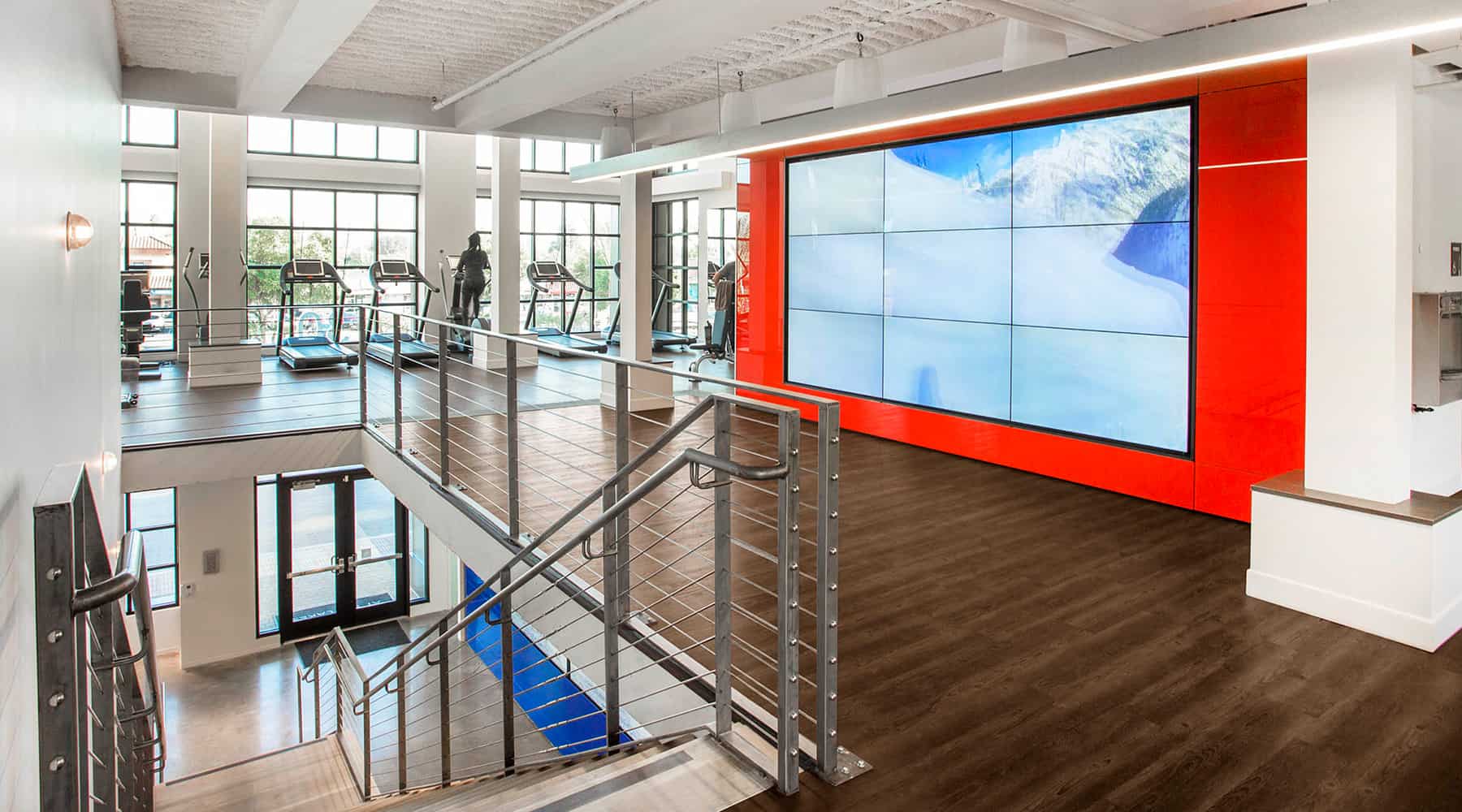 Spacious gym with cardio machines and large windows for natural light.