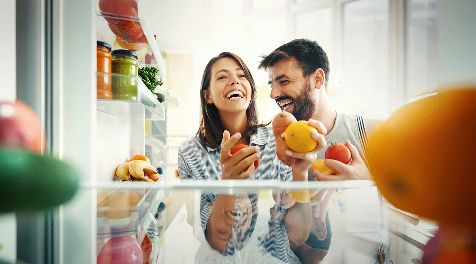 Happy couple laughing while shopping and holding fruits in a bright kitchen.