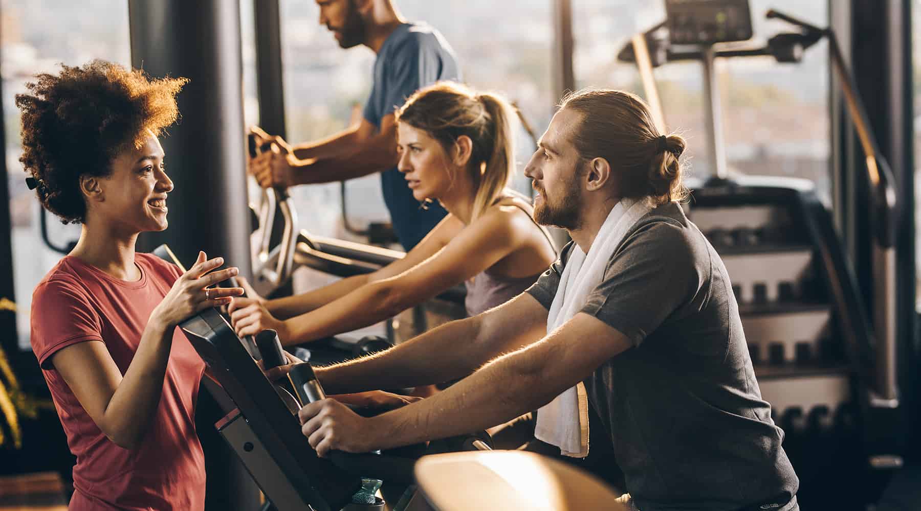 People exercising on ellipticals and having a conversation at the gym.