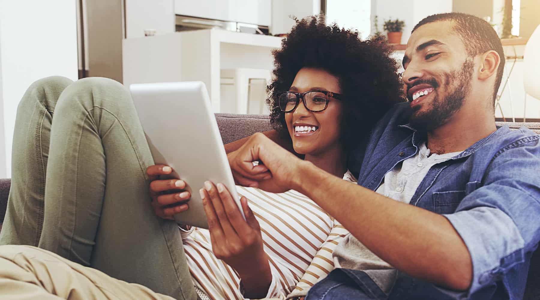 Couple laughing together while looking at a tablet on the couch.