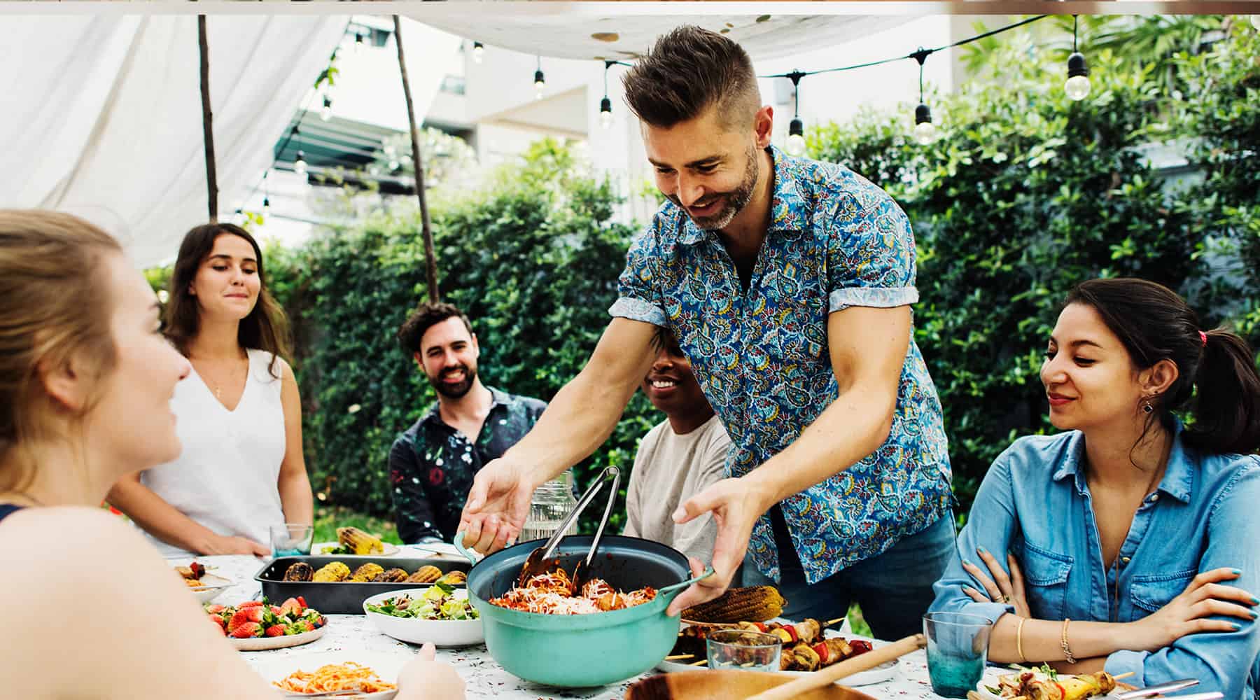 Group of people enjoying a social gathering outdoors, sharing a meal and having a good time.