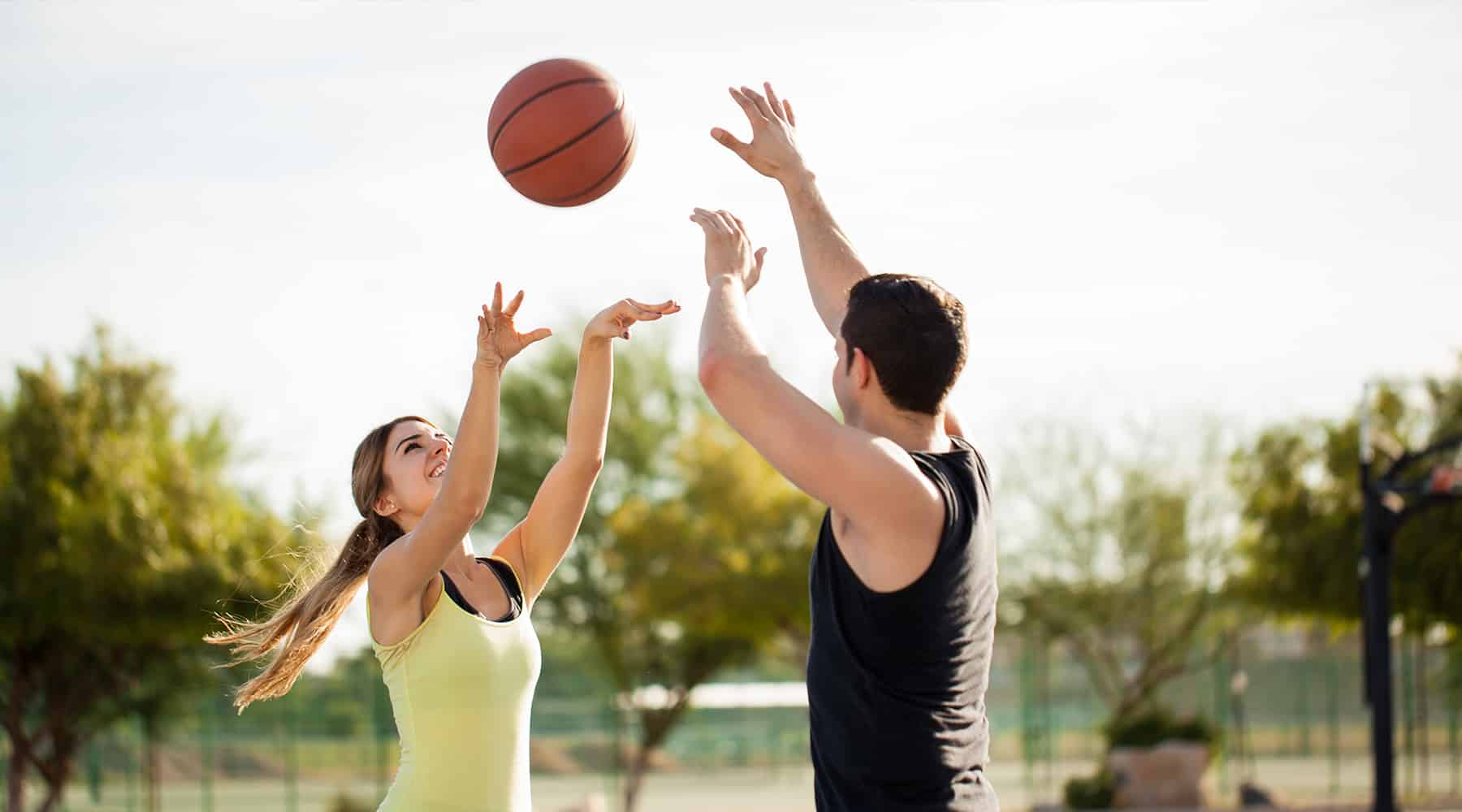 Person shooting a basketball in a park on a sunny day.