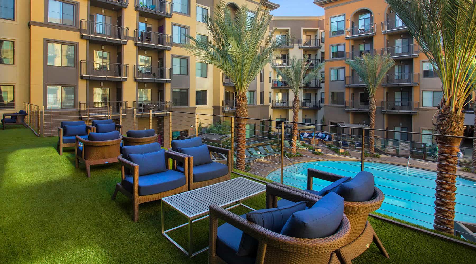 Apartment complex with palm trees and poolside seating area.