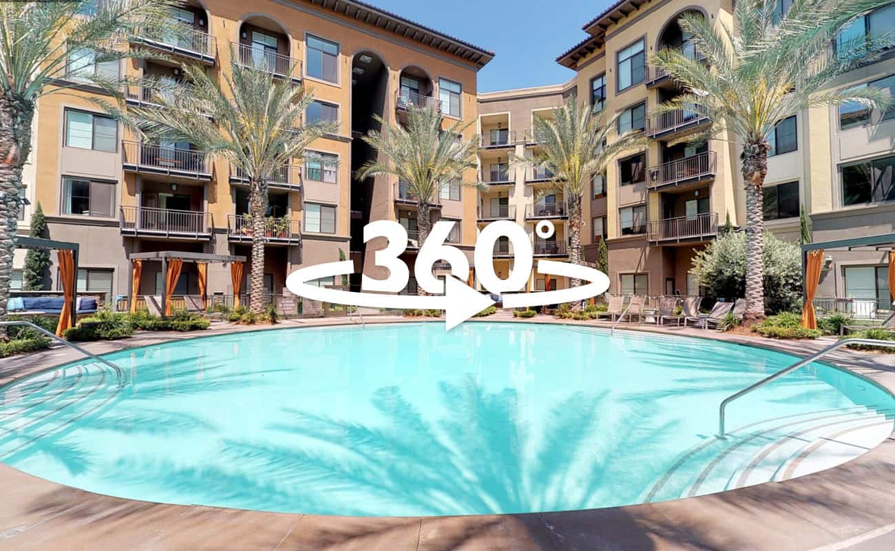 360-degree view of the pool area surrounded by lounge chairs, palm trees, and apartment buildings.