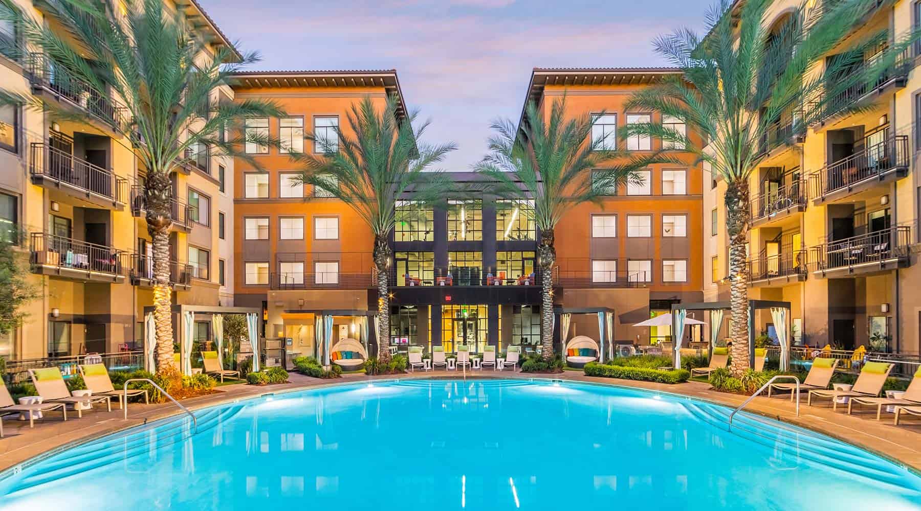 Resort-style apartment pool with lounge chairs and palm trees.