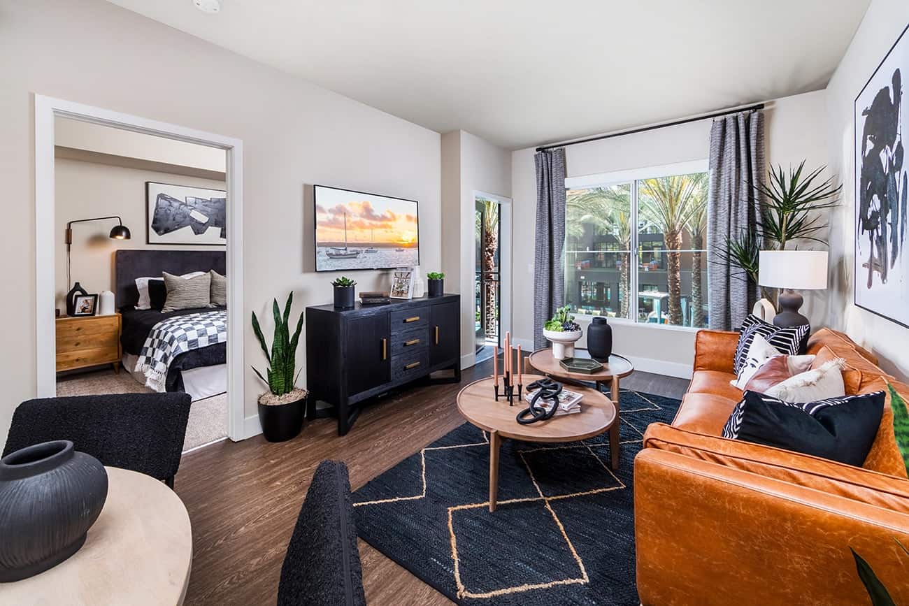 Colony at the Lakes - Plan A4 - Stylish living room with a large couch, a wooden coffee table, and a bedroom visible in the background.