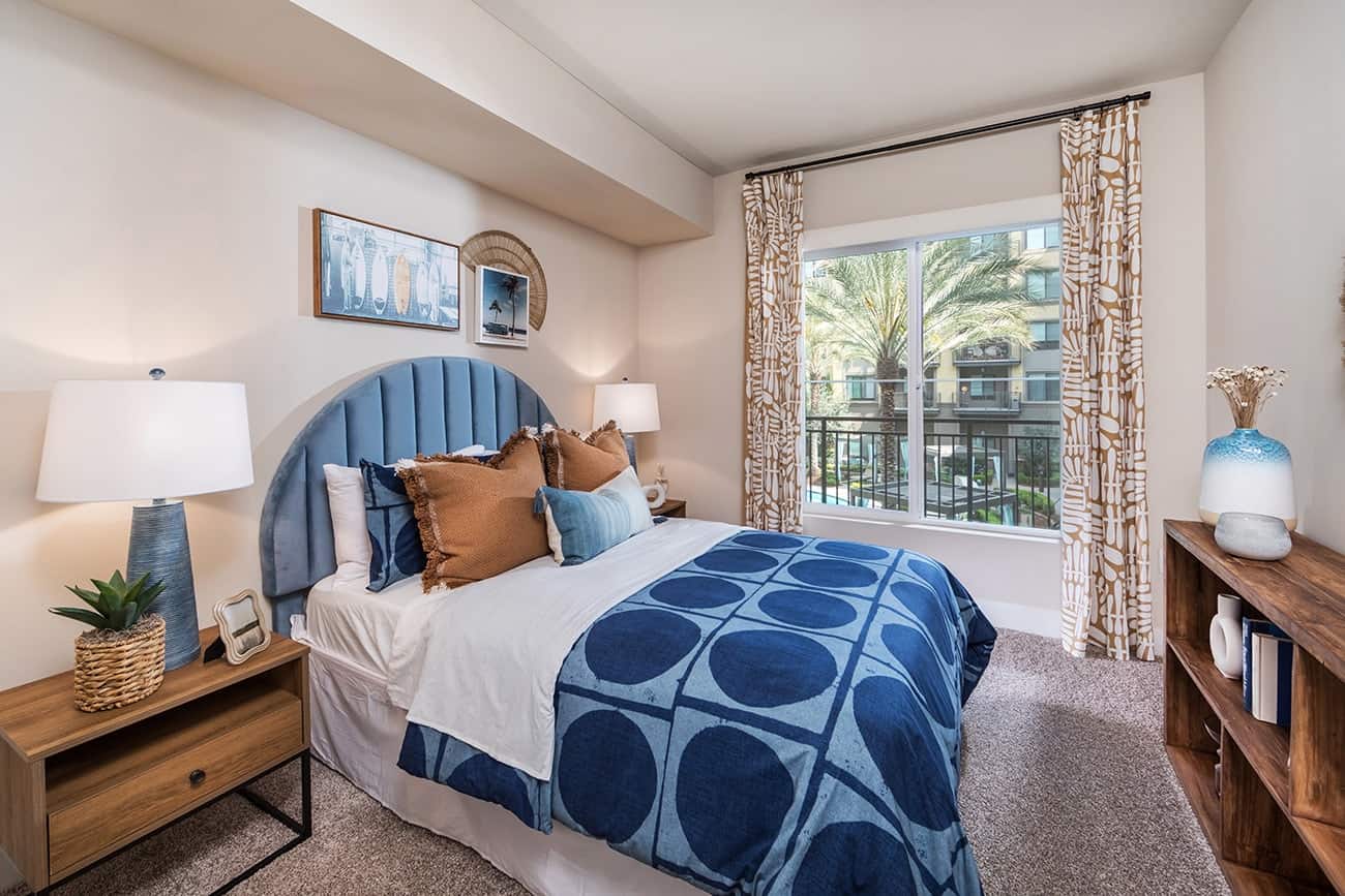Colony at the Lakes - Plan B1 - Comfortable bedroom with a blue bedspread and natural light from the window.
